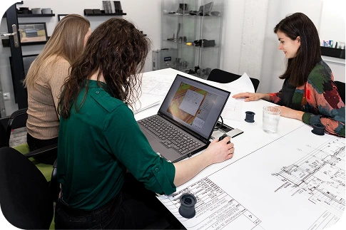 Das Expertenteam von Silencions – drei Personen, die an einem Tisch sitzen und technische Pläne sowie Ergebnisse von Akustiksimulationen auf einem Laptopbildschirm analysieren.