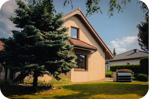 Einfamilienhaus mit beiger Fassade und orangefarbenem Dach. Neben dem Haus, auf dem Rasen, befindet sich eine Wärmepumpe mit einer modernen Silencions-Schallschutzhaube für Wärmepumpen.