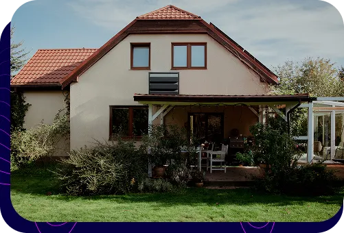 Dieses Einfamilienhaus besticht durch seine beige Außenfassade und das braune Dach. An der Gebäudewand ist eine dunkle Silencions s|AC|-Schallschutzhaube montiert, die die Außeneinheit der Klimaanlage schützt.