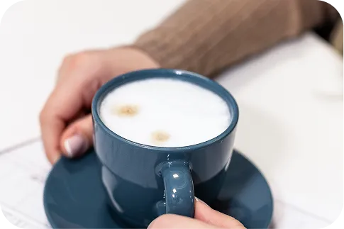 Hände halten eine blaue Tasse Kaffee mit Schaum, die Komfort und Ruhe in der Büroumgebung symbolisiert, ermöglicht durch eine leise Klimaanlage.