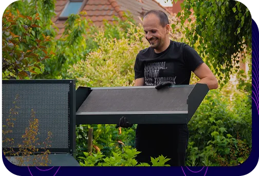 Mann im Garten, der den oberen Abschnitt der dunklen Silencions s|AC|-Schallschutzkabine installiert, lächelt und demonstriert, wie einfach die Installation ist.