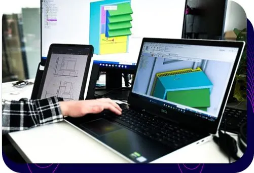 Der Ingenieur Silencions arbeitet im Rahmen des Programms an einem Projekt für ein Gehäuse für eine Wärmepumpe; auf dem Laptop-Bildschirm und dem Monitor sind ein 3D-Modell und eine technische Zeichnung zu sehen.