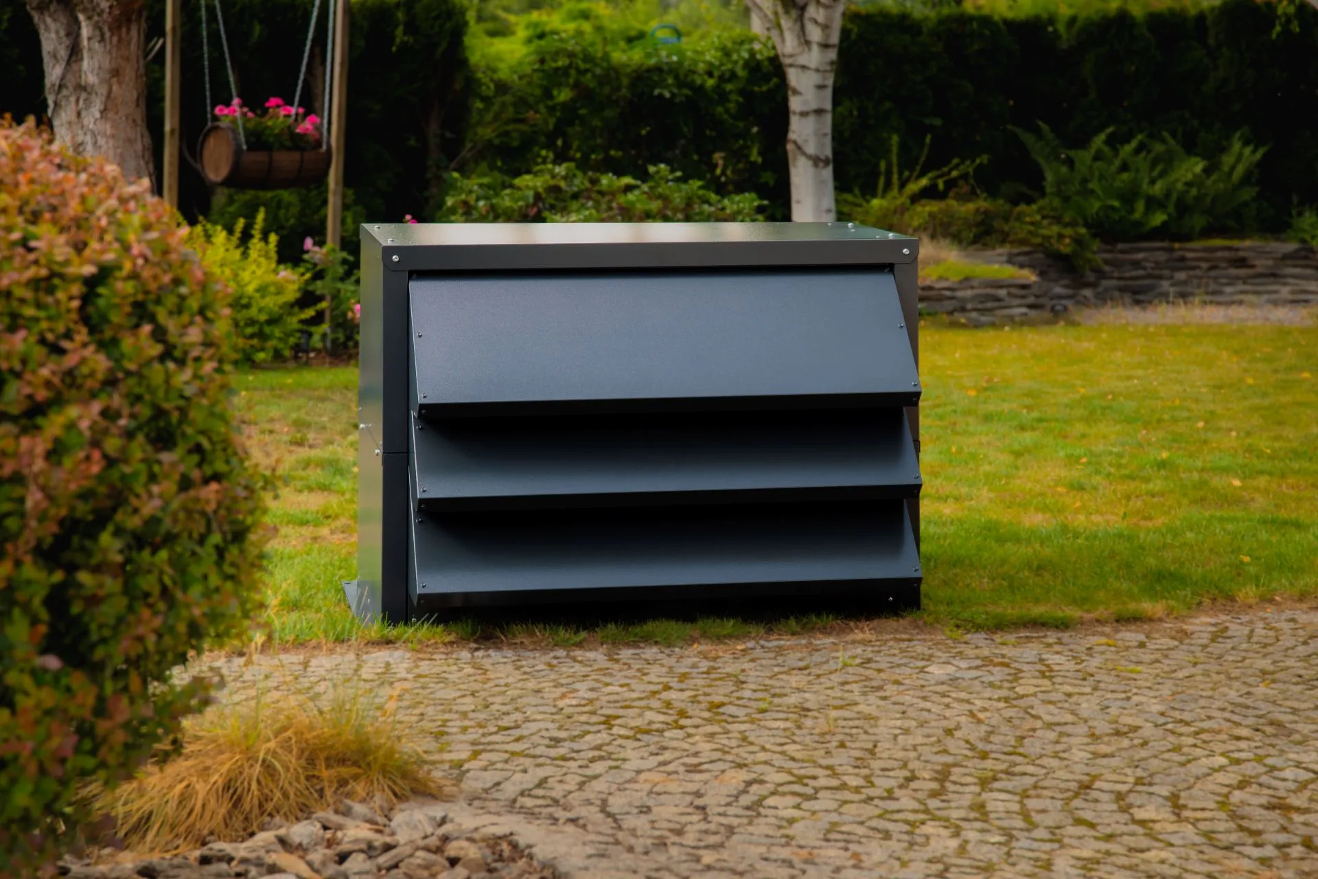 Wärmepumpe in einem modernen, graphitfarbenen Silencions-Schallschutzgehäuse, aufgestellt auf dem Rasen neben der gepflasterten Auffahrt.